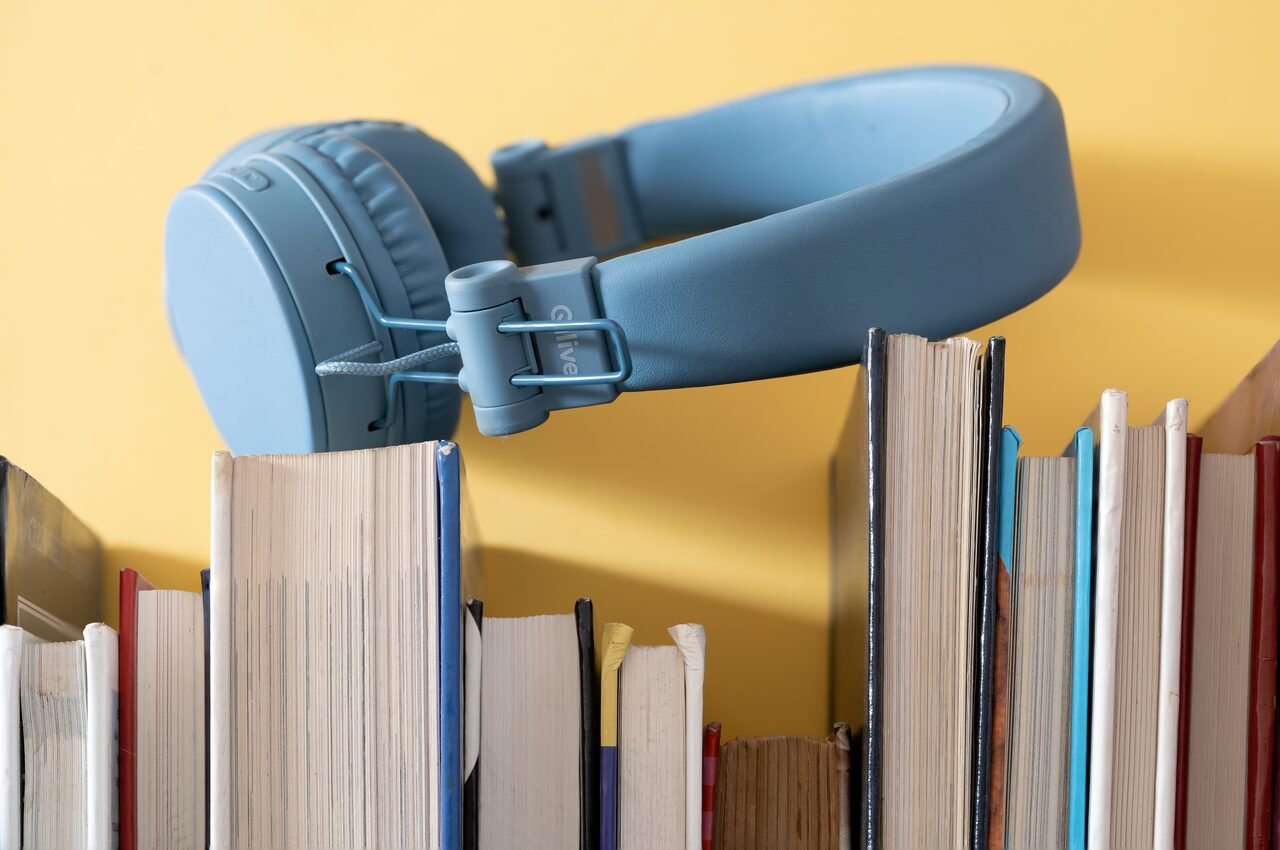 Blue headphones rest on a stack of books against a yellow background, symbolizing leisure and learning.