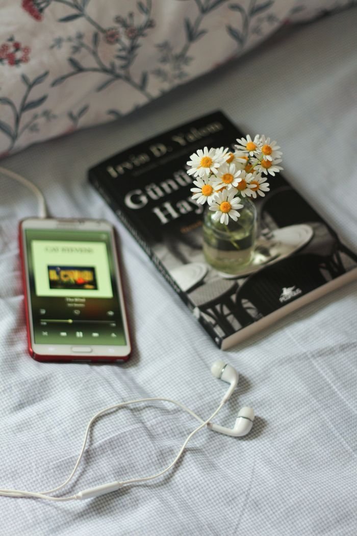 A peaceful composition featuring daisies, a book, and a smartphone with earphones.